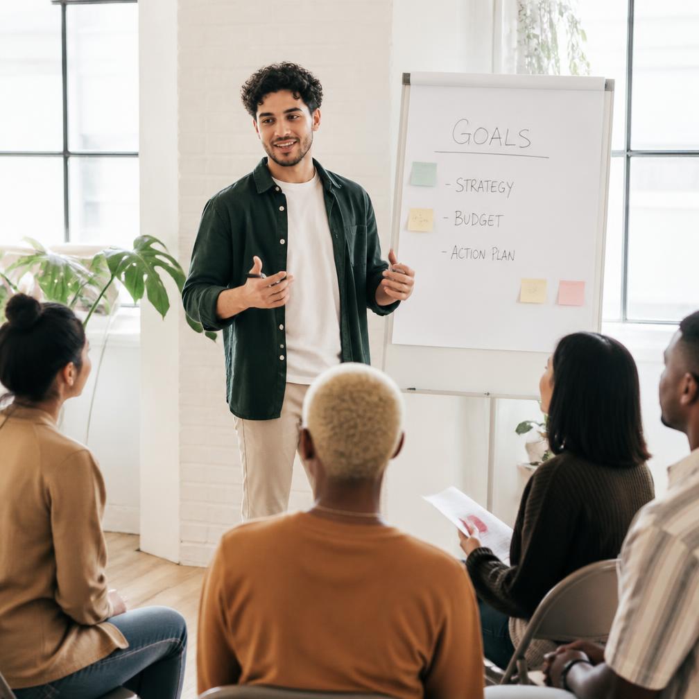 A trainer explaining a topic to a small group in a bright room.